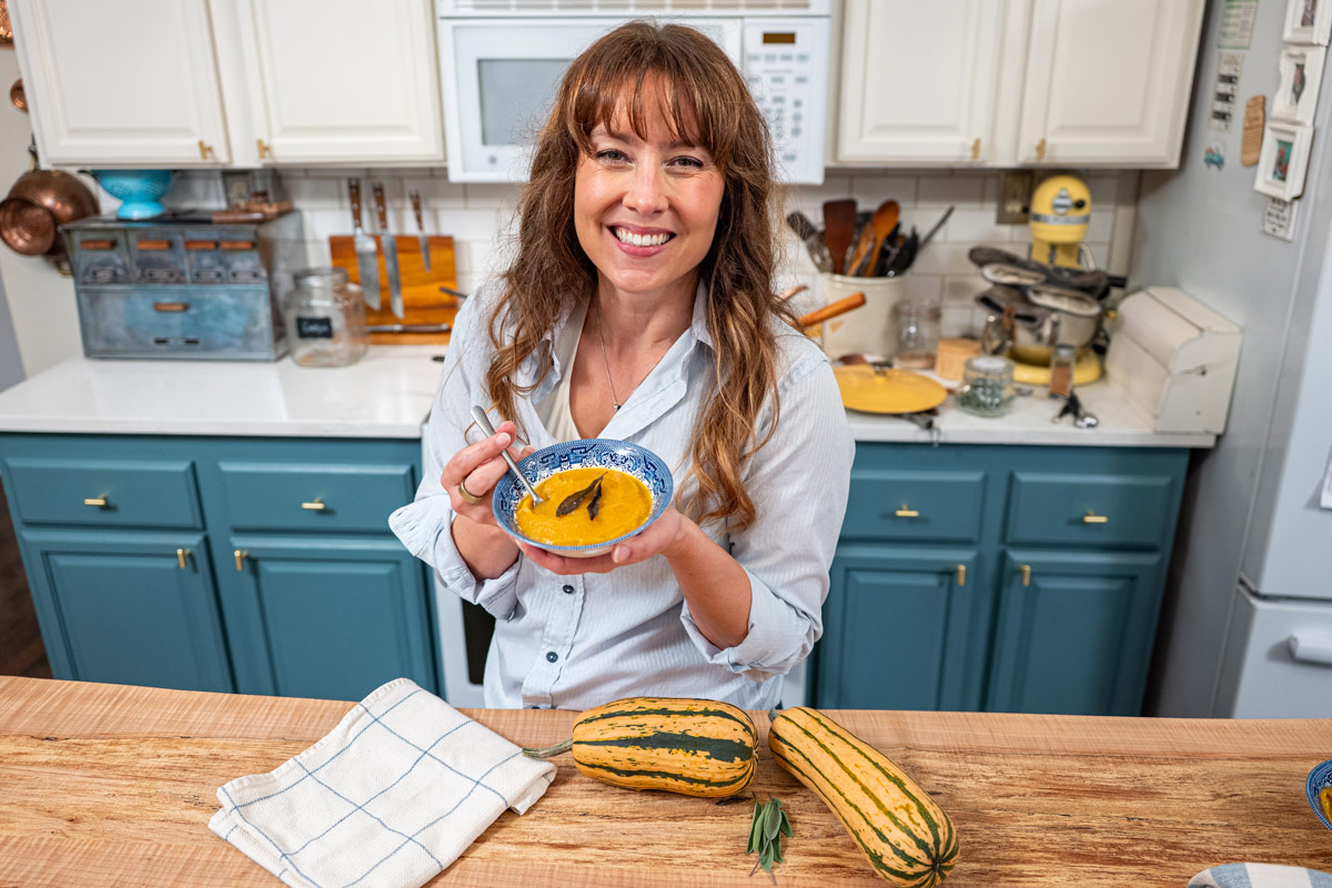 A woman holding a bowl of delicata squash soup.