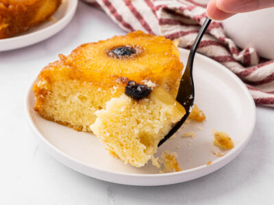 A slice of pineapple upside down cake with a bite on a fork to show texture.