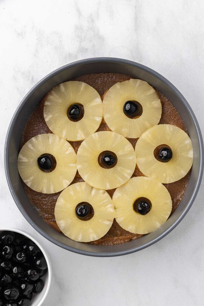 A cake pan prepared with brown sugar topping, slices of pineapple and cherries.
