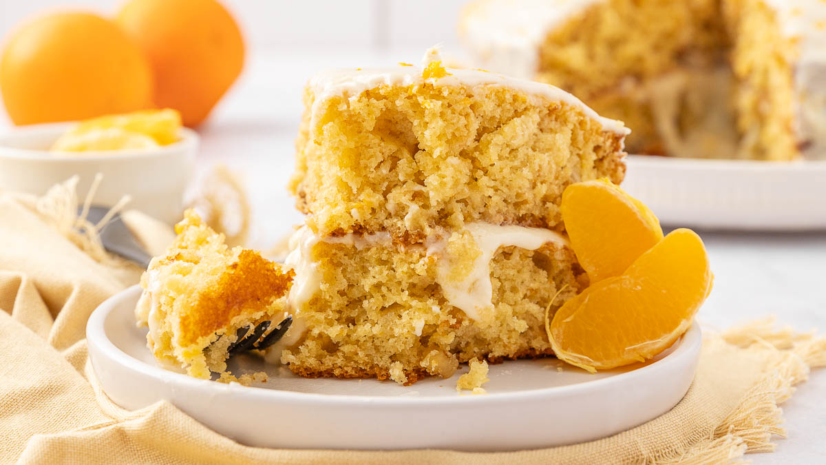 A slice of tangerine cake on a white plate garnished with segmented tangerines.