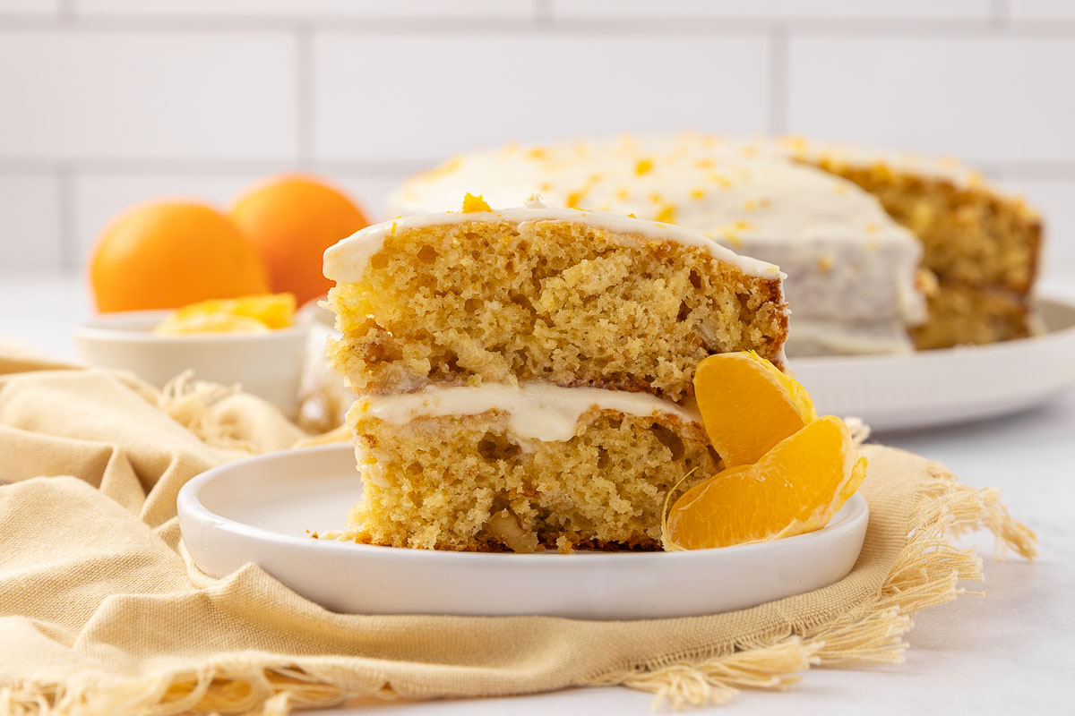 A slice of tangerine cake on a white plate garnished with segmented tangerines.