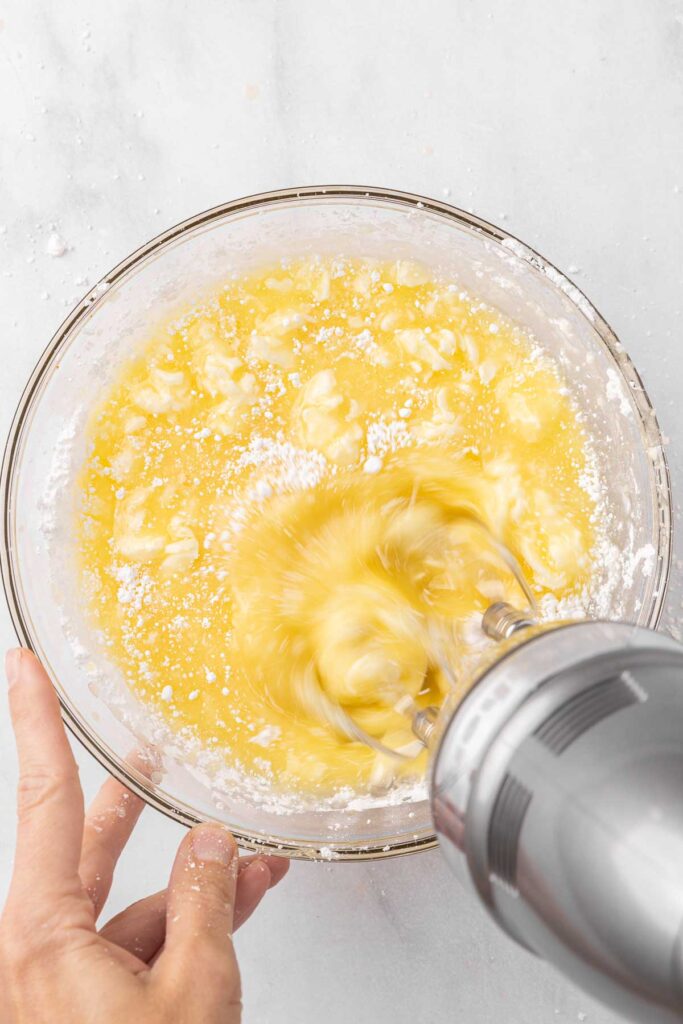 A hand mixer blending together citrus frosting for tangerine cake.