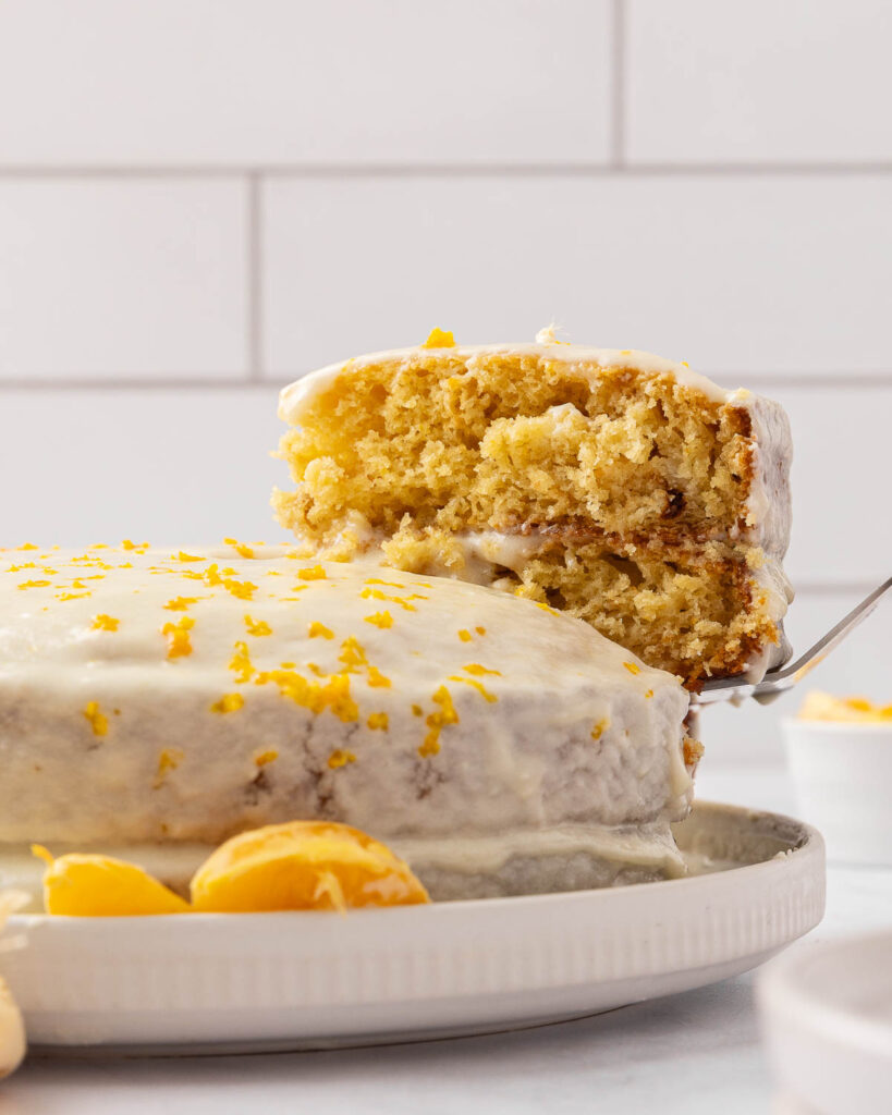 Tangerine cake on a serving platter with a cake server removing a slice to show texture.