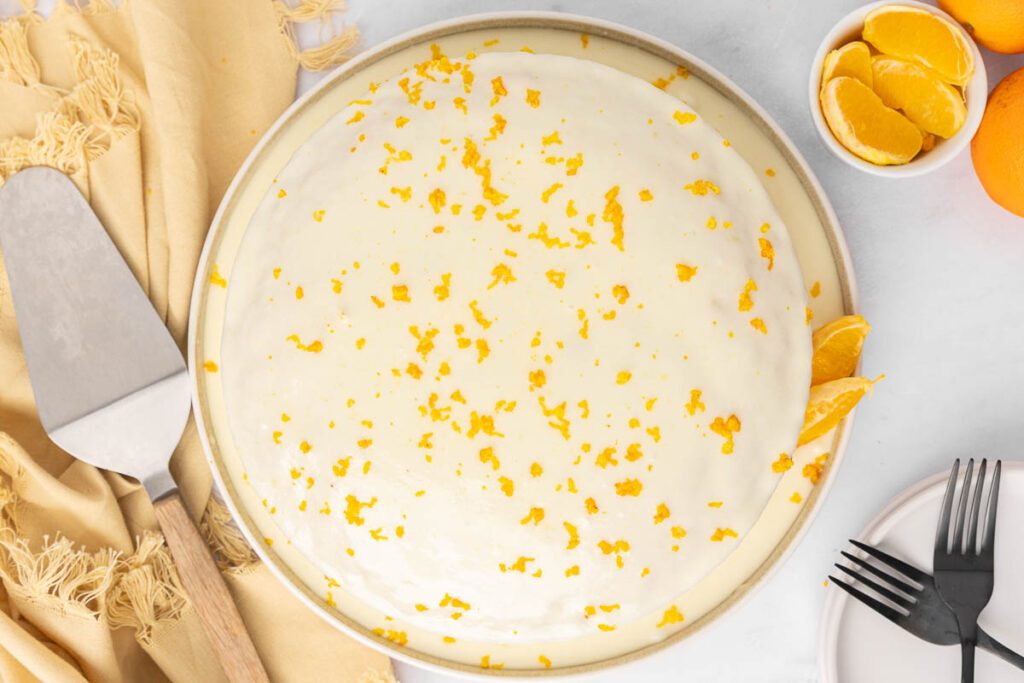 A bird's eye view of a frosted tangerine cake garnished with tangerine zest.