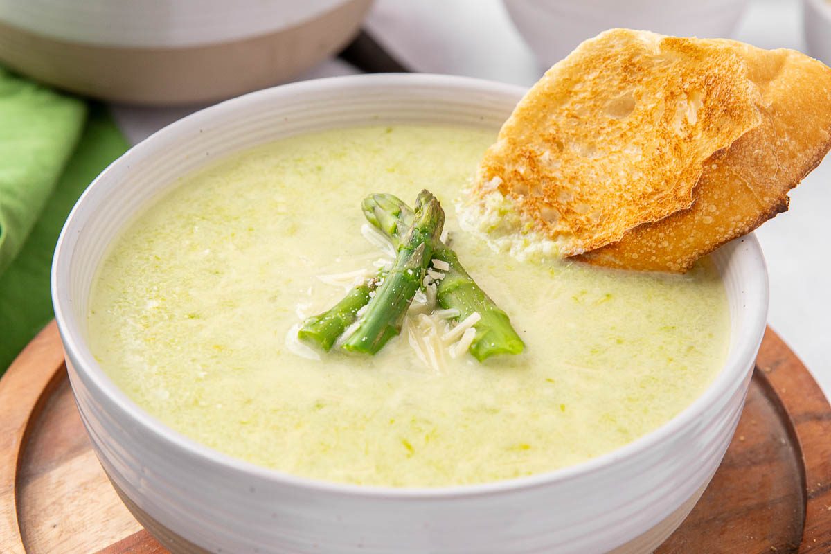 A bowl of creamy asparagus soup garnished with asparagus spears and garlic toast.