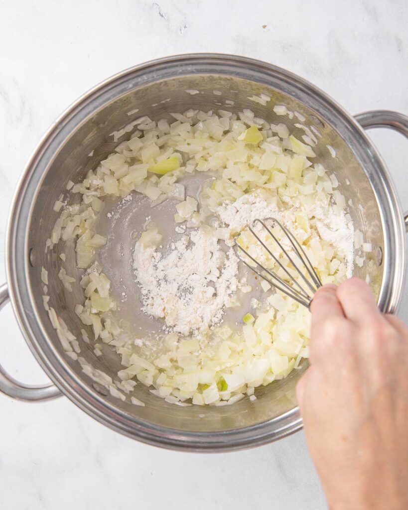 Whisking flour into a pan with sauteed onions and garlic.