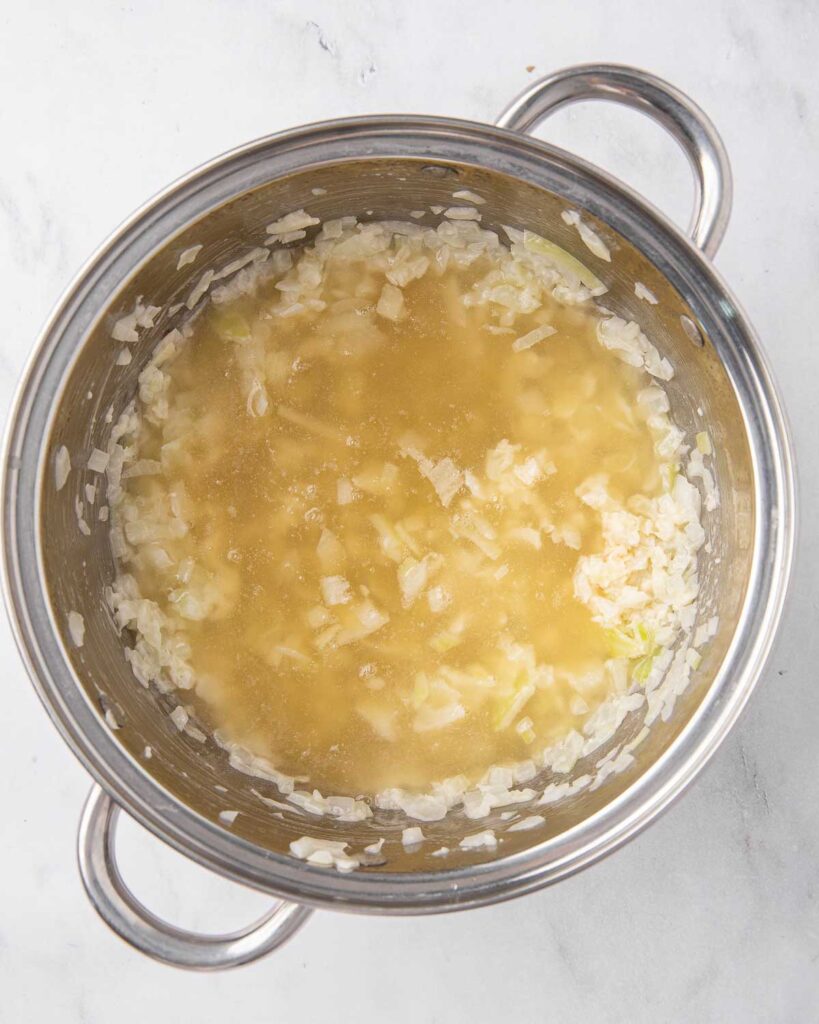 Chicken broth added to sauteed onions, garlic, and flour in a pan to make a roux.