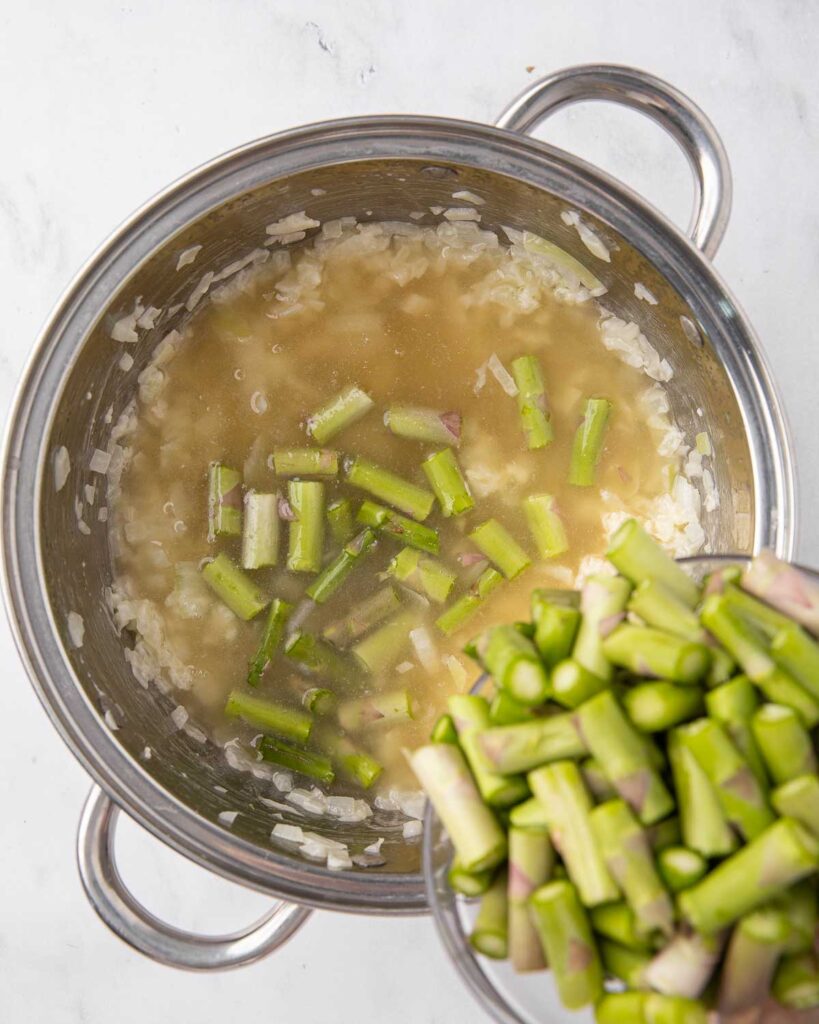 Adding asparagus to chicken broth and onion mixture in a saucepan.