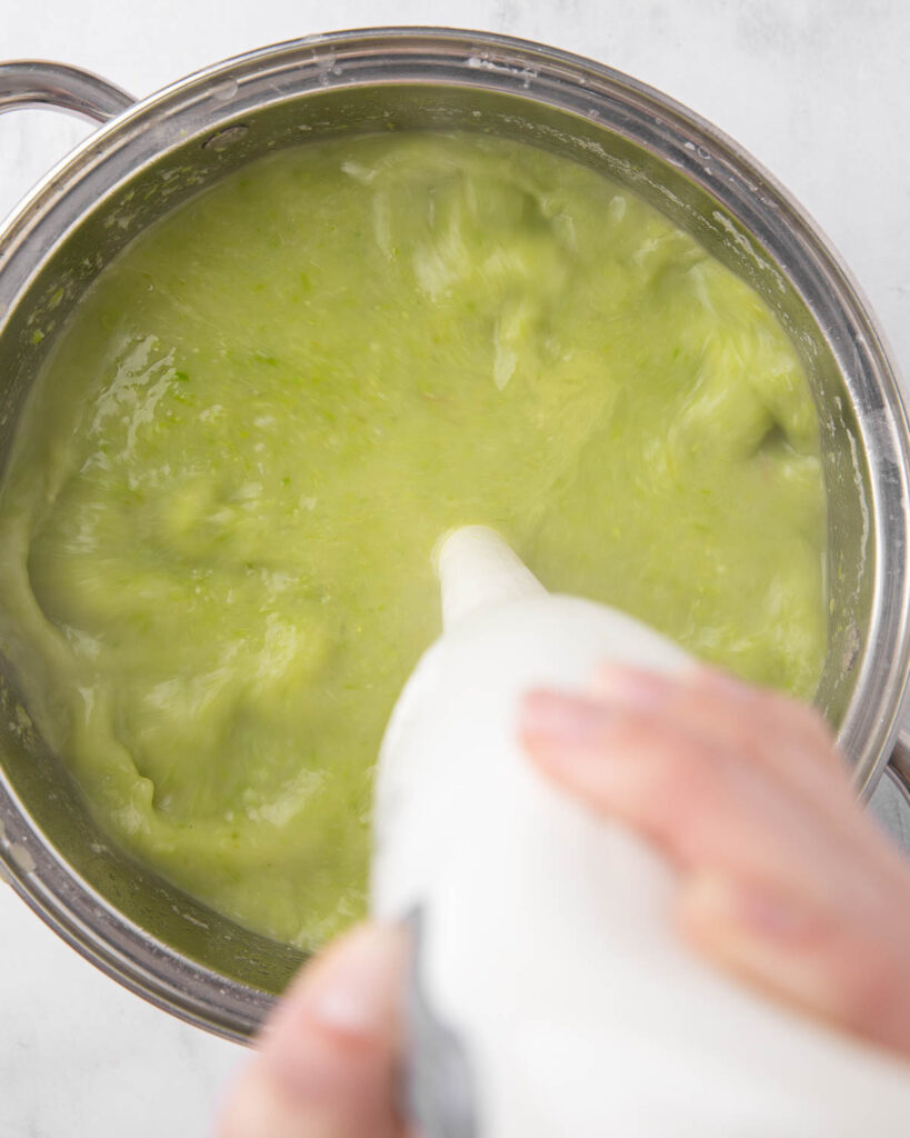 An immersion blender, blending asparagus soup in a saucepan.