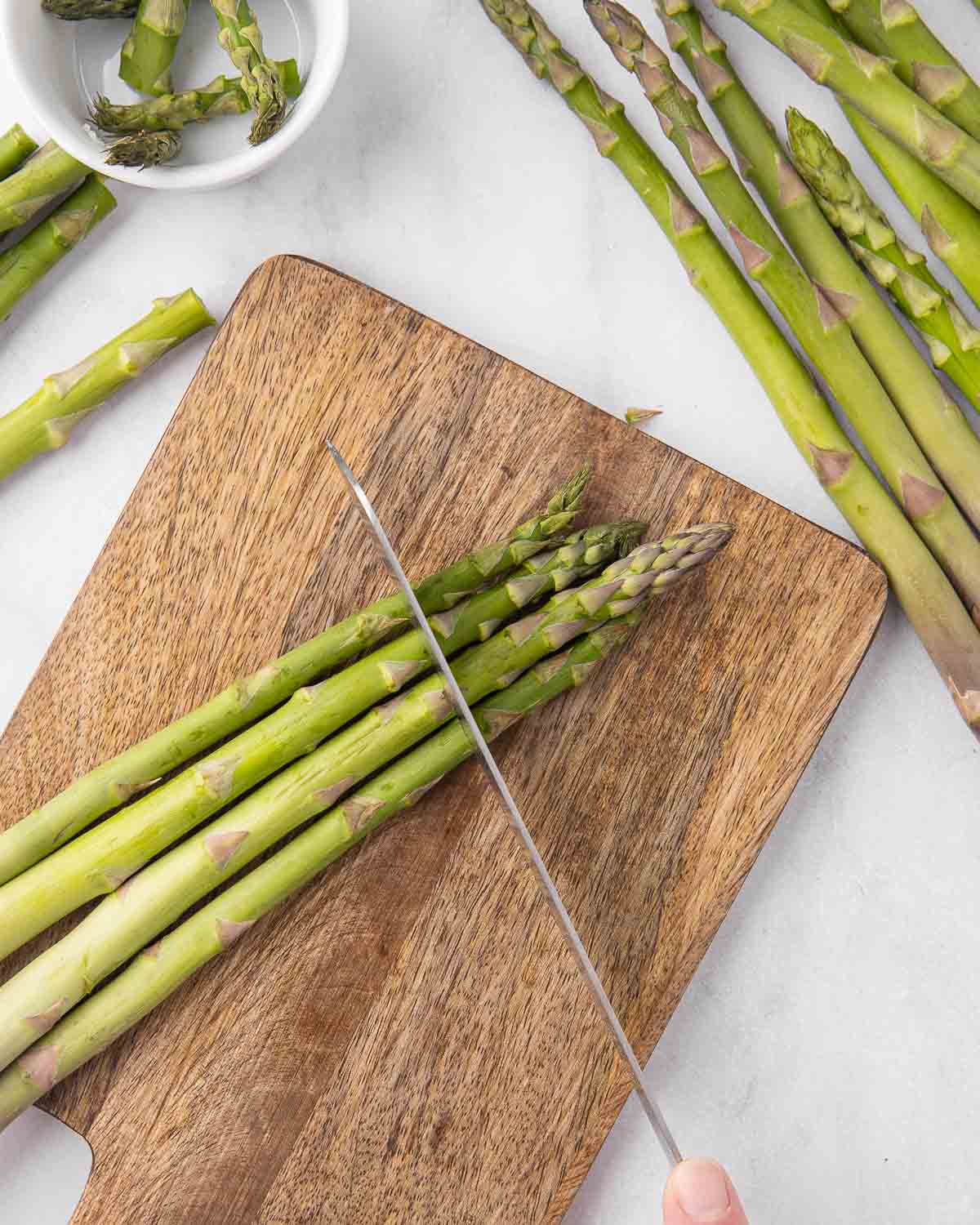 A knife removing asparagus tips on a cutting board.