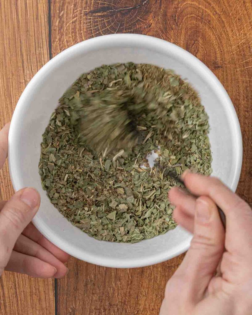 A fork mixing Italian seasoning mix ingredients in a small bowl.