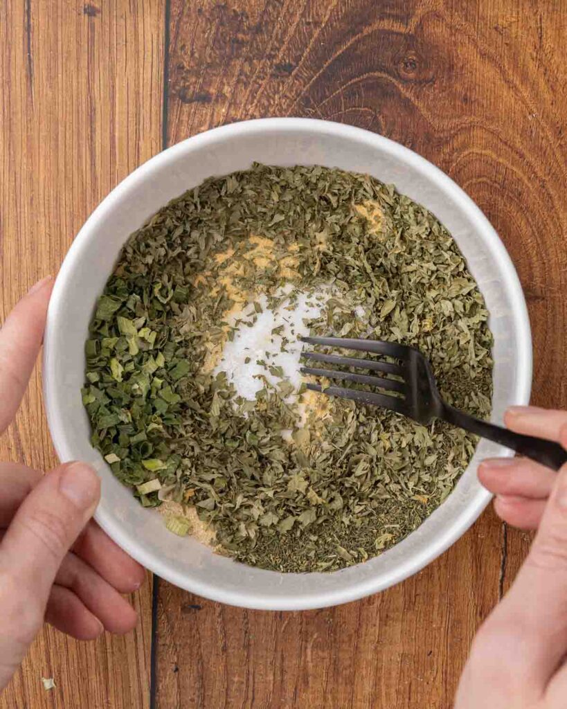 A fork mixing ranch seasoning mix ingredients in a small bowl.