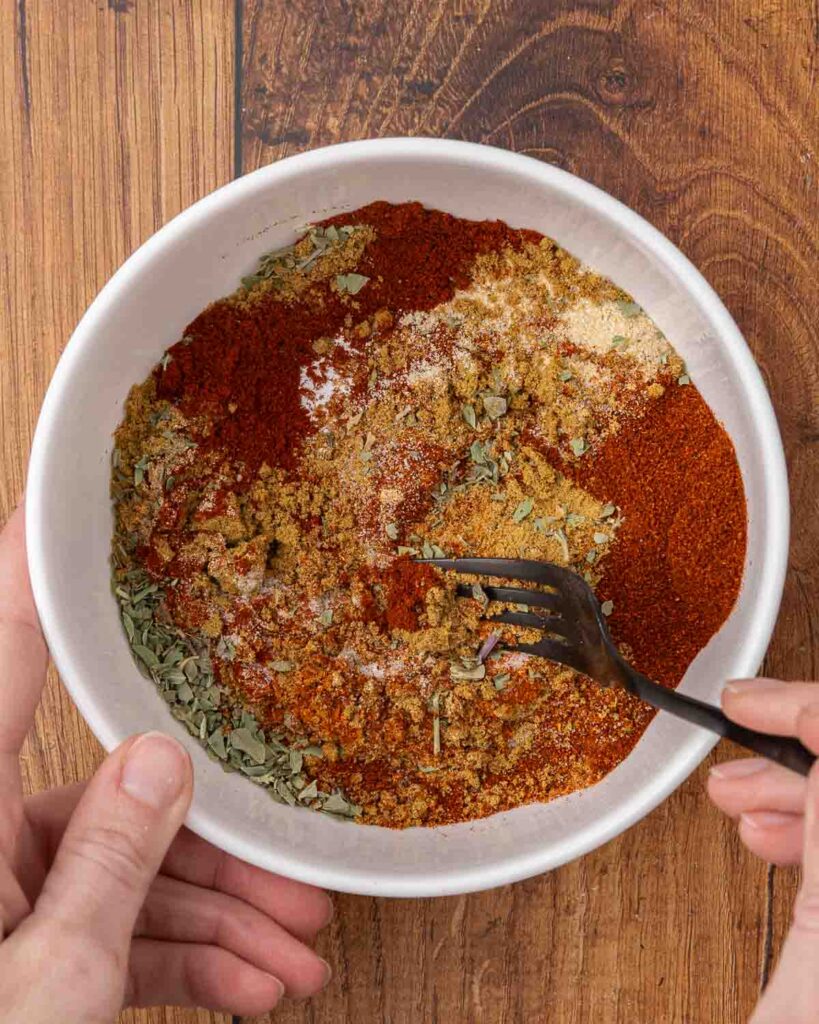 A fork mixing taco seasoning mix ingredients in a small bowl.