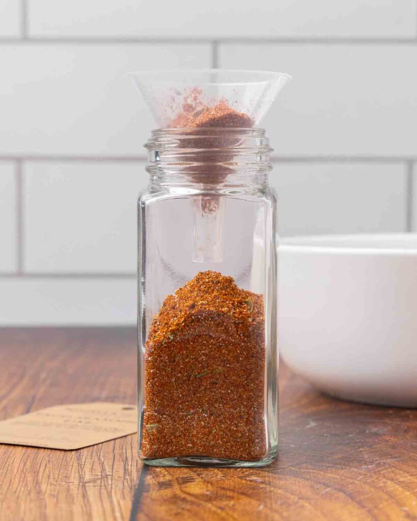 A jar topped with a funnel being filled with DIY taco seasoning mix.