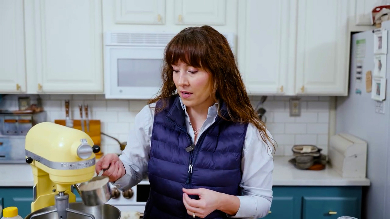 A woman adding ingredients to a stand mixer for homemade graham crackers.