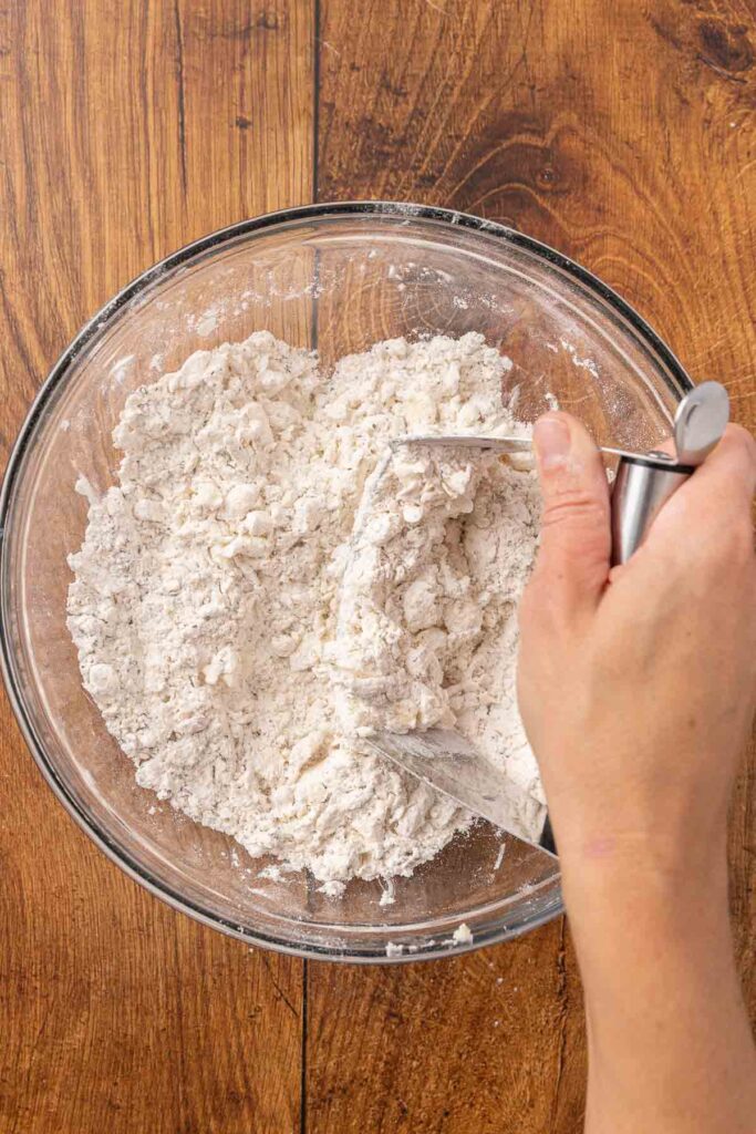 A pastry cutter, cutting butter into flour in a glass bowl.