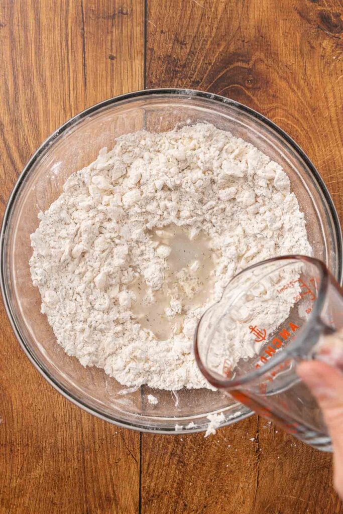 Pouring water and honey into a bowl full of flour and butter mixture.