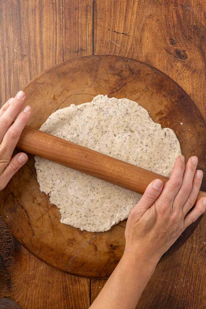 Hands using a rolling pin to roll out cracker dough onto a pizza stone.