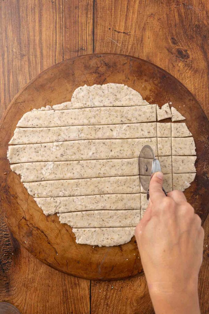 Hands using a pizza cutter to cut cracker dough into pieces.