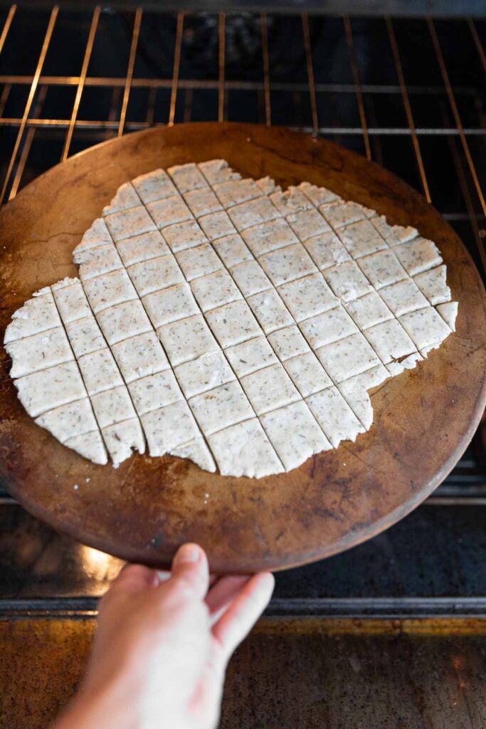 A pizza stone with cracker dough going into the oven.