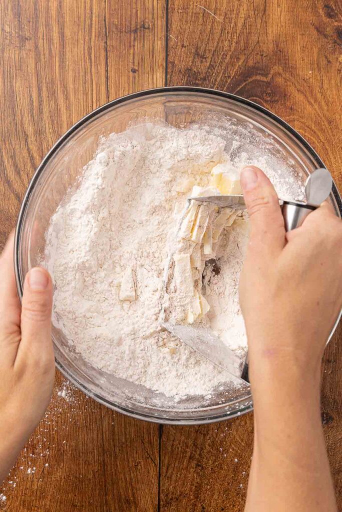 A pastry cutter, cutting butter into flour in a glass bowl.