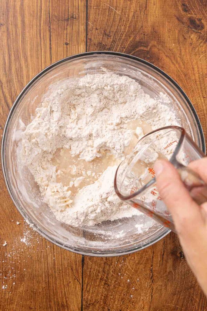 Pouring water and honey into a bowl full of flour and butter mixture.
