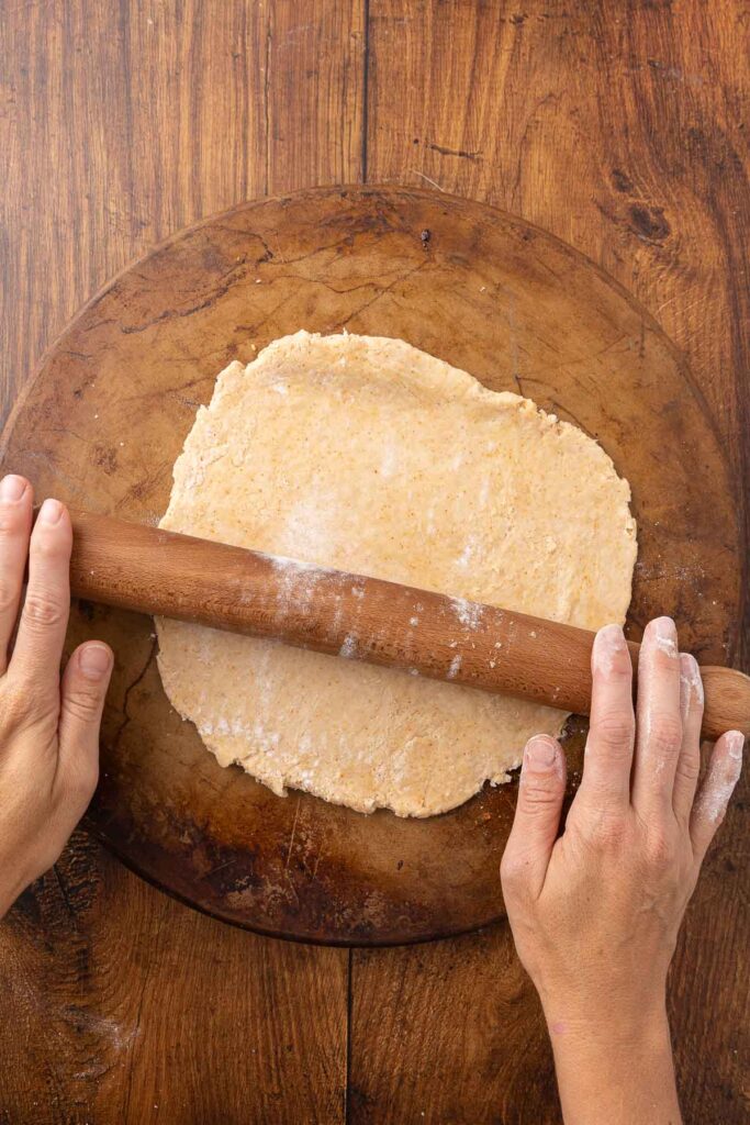 Hands using a rolling pin to roll out cracker dough onto a pizza stone.