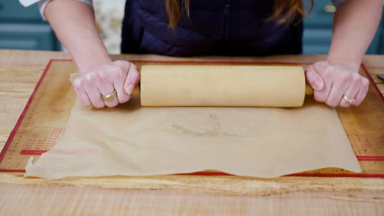Rolling graham cracker dough between parchment paper with a rolling pin.