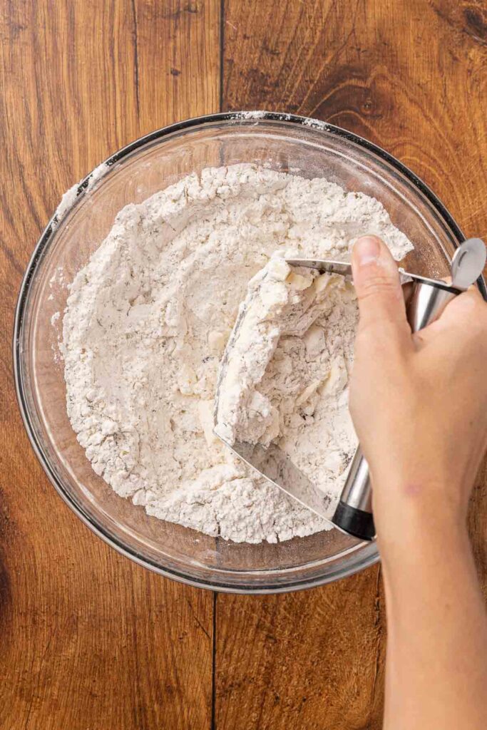 A pastry cutter, cutting butter into flour in a glass bowl.
