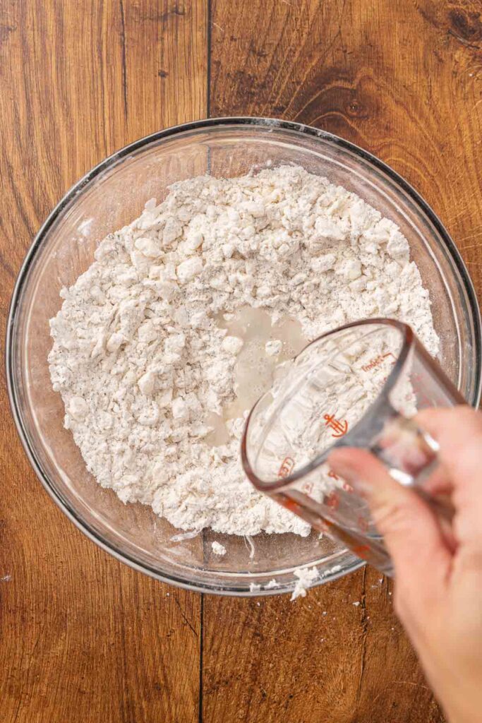 Pouring water and honey into a bowl full of flour and butter mixture.
