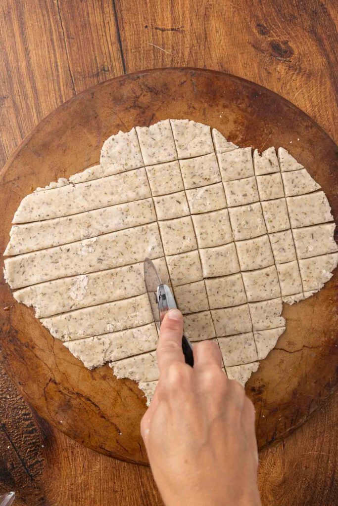 Hands using a pizza cutter to cut cracker dough into pieces.
