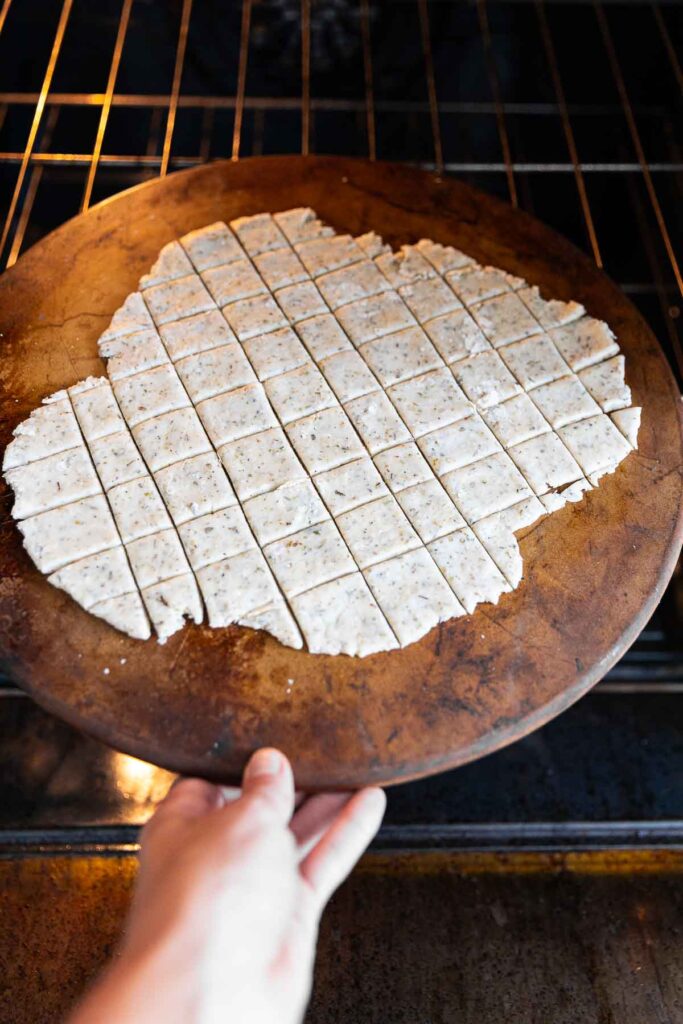 A pizza stone with cracker dough going into the oven.
