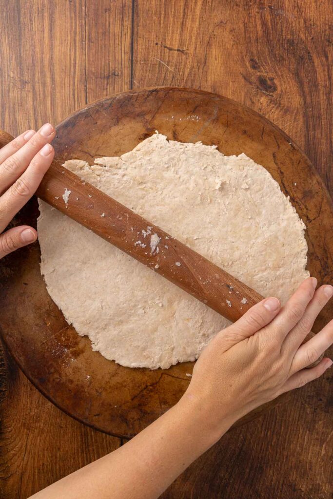 Hands using a rolling pin to roll out cracker dough onto a pizza stone.