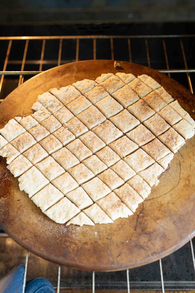 A pizza stone with cracker dough going into the oven.