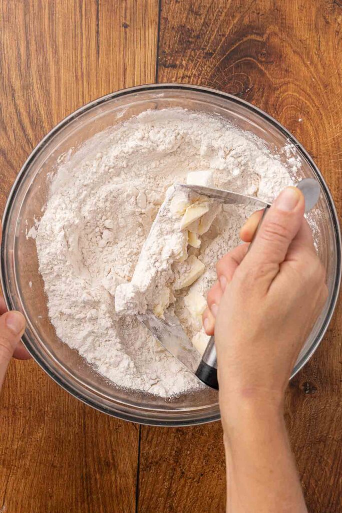 A pastry cutter, cutting butter into flour in a glass bowl.