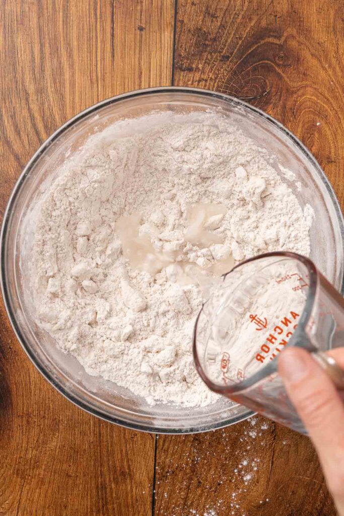 Pouring water and honey into a bowl full of flour and butter mixture.