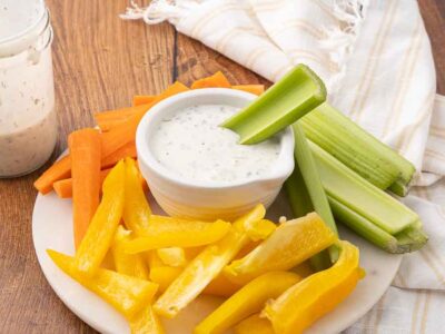 A platter of veggies circled around a bowl of homemade buttermilk ranch dressing.
