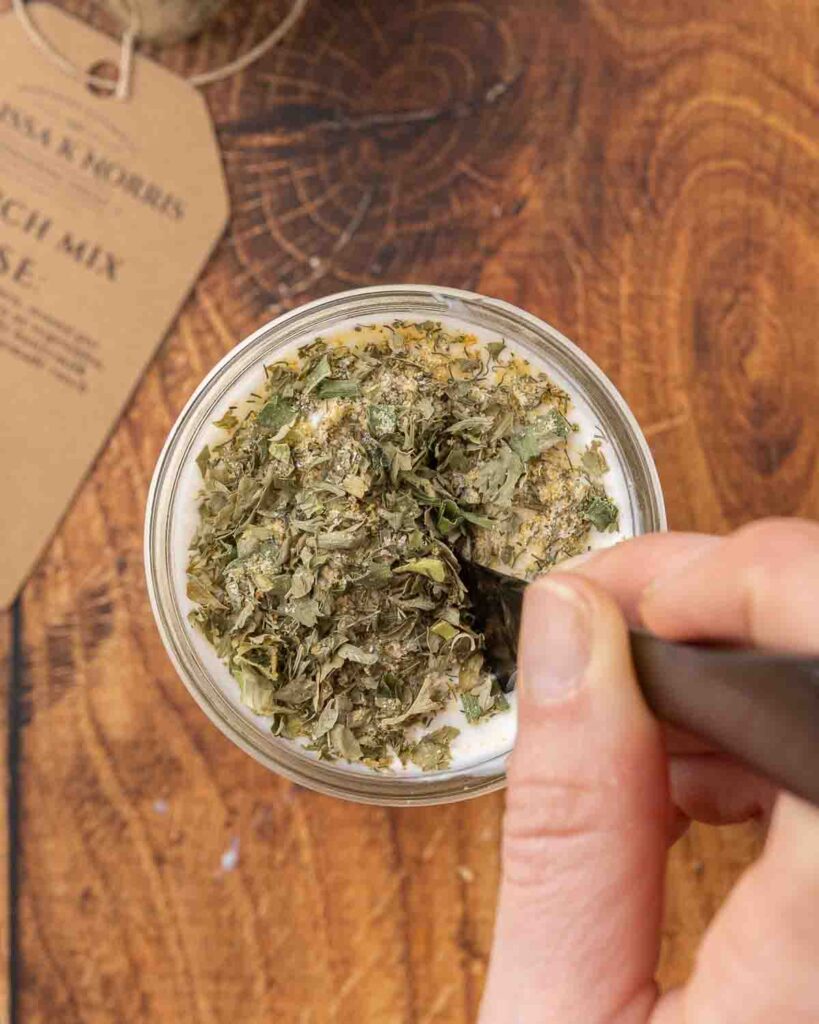 Mixing ranch seasoning into a jar filled with buttermilk, mayo, sour cream, garlic, and lemon juice.