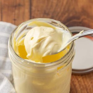 A spoon lifting homemade mayonnaise from a jar to show texture.