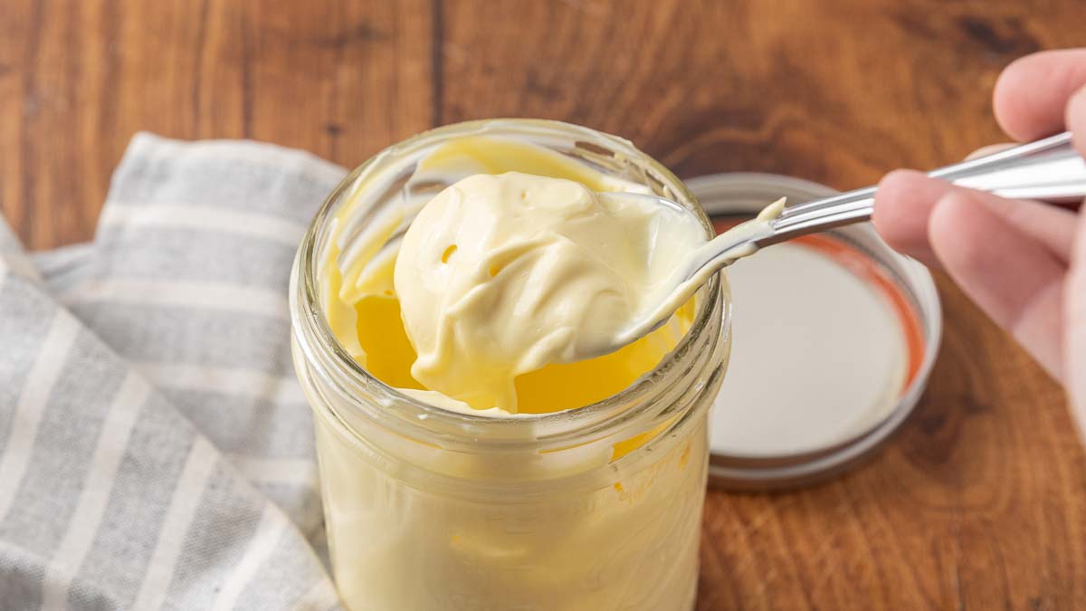 A spoon lifting homemade mayonnaise from a jar to show texture.