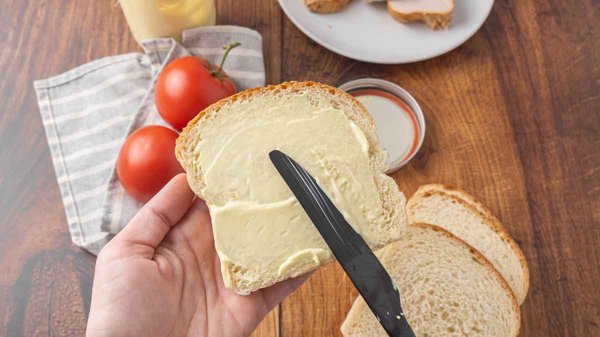 A knife spreading homemade mayonnaise on a slice of bread.
