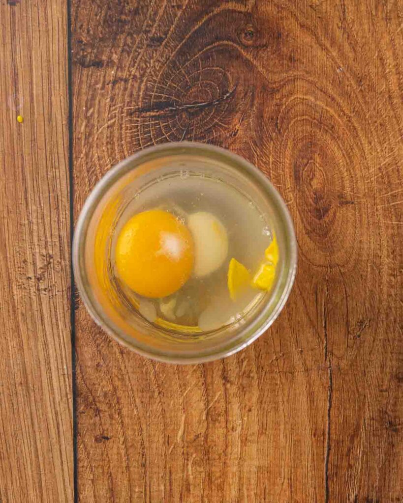 Bird's eye view of a glass mason jar with an egg, mustard, salt, lemon juice, and white vinegar.
