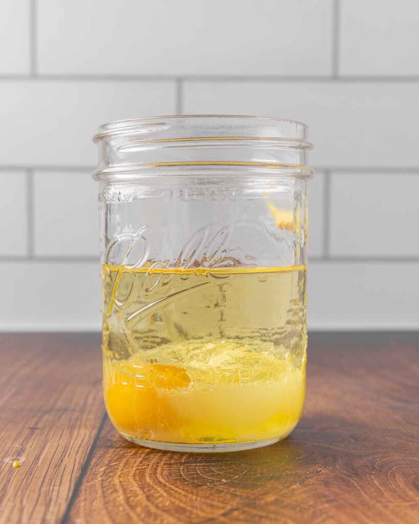 A Mason jar filled with an egg, mustard, lemon juice, vinegar, salt, and oil. Side view to show the oil settling to the top.