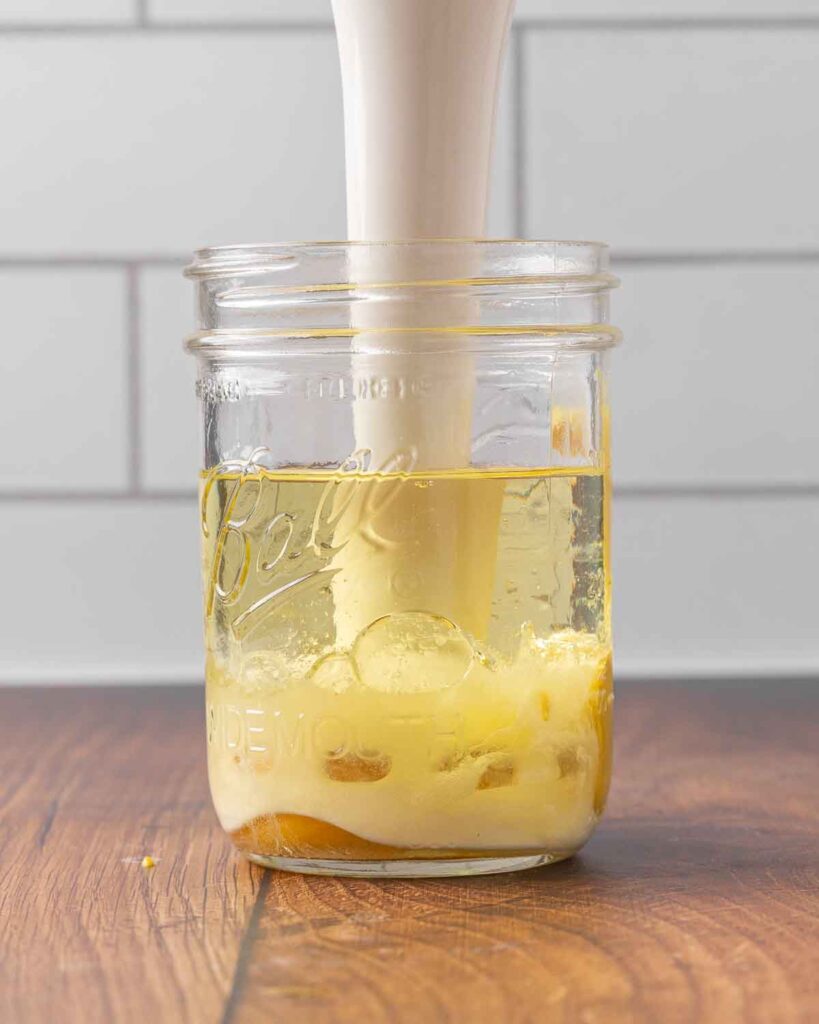 An immersion blender blending mayo ingredients in a jar.