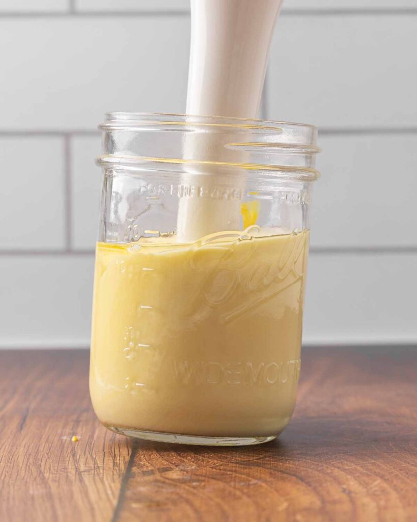 An immersion blender blending mayo ingredients in a jar.