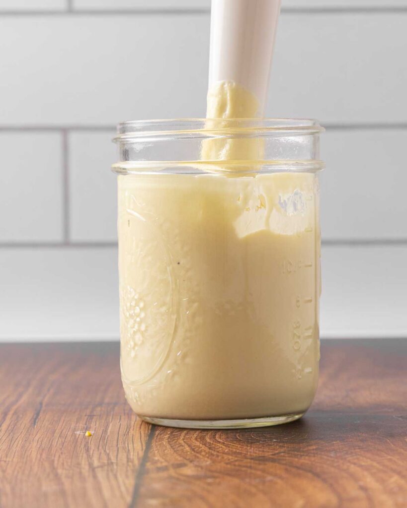 An immersion blender blending mayo ingredients in a jar.