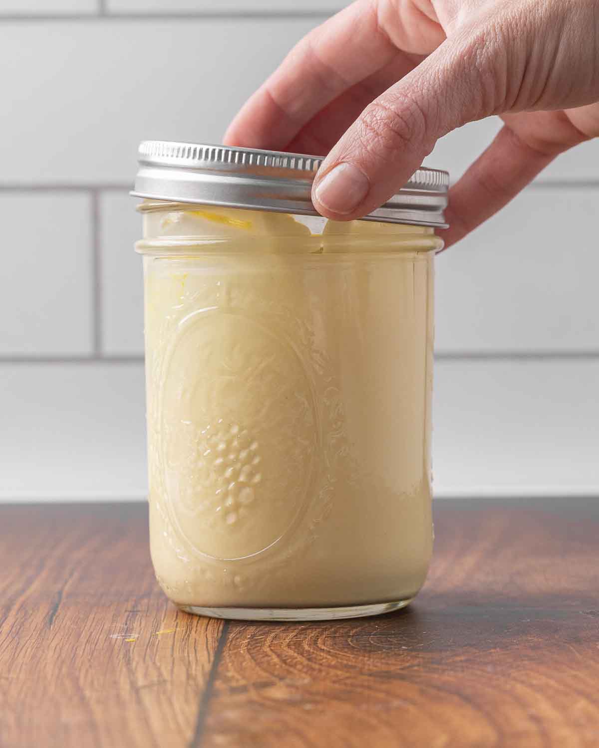 A hand placing a lid on a jar full of homemade mayonnaise.