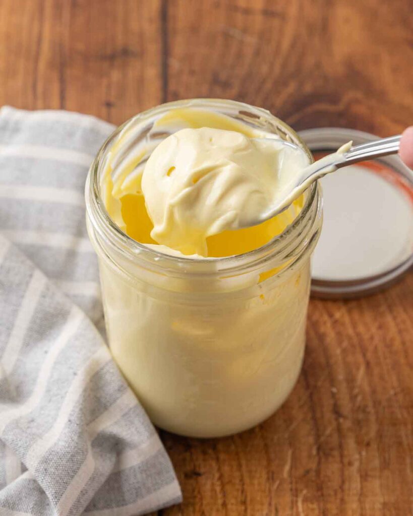 A spoon lifting homemade mayonnaise from a jar to show texture.