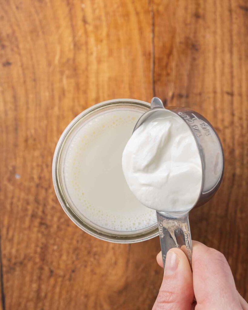 A small amount of cooled milk in a bowl with a spoon adding yogurt starter cultures.
