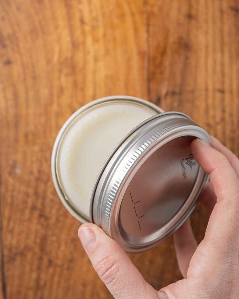 A hand placing a lid on top of a glass jar full of homemade yogurt.